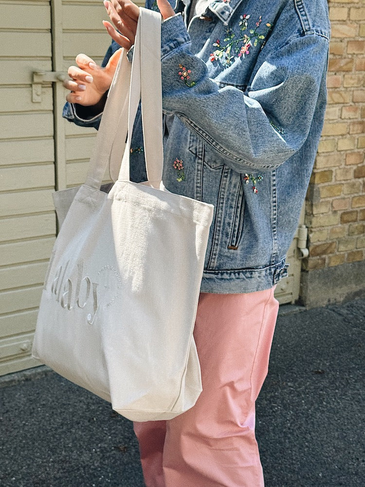 Woman holding a Lalaby Toto tote bag in a natural beige color, made from organic cotton, for everyday use