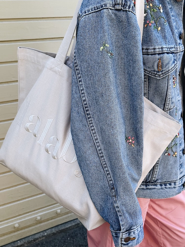 Woman holding a Lalaby Toto tote bag in a natural beige color, made from organic cotton, for everyday use